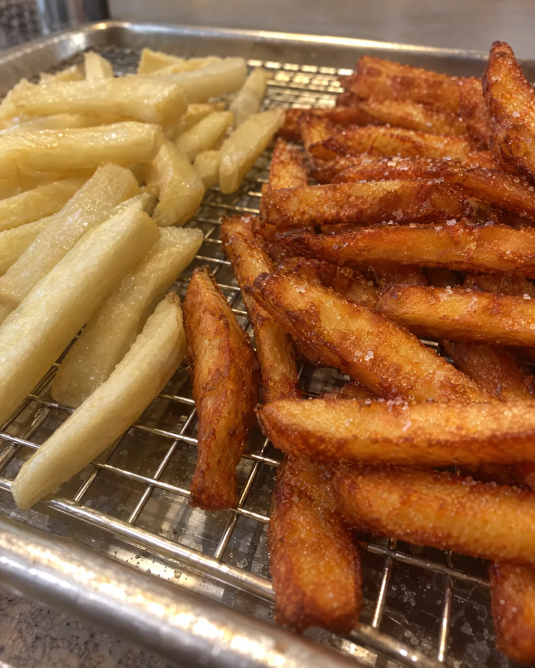 Pale once-fried potatoes on a rack next to golden twice-fried fries