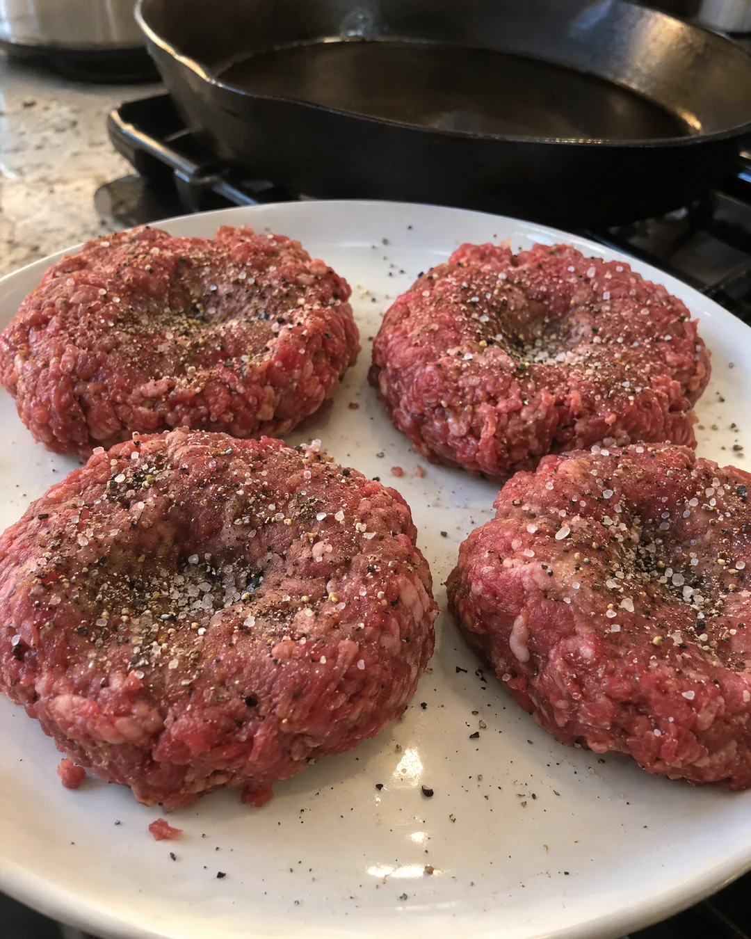 Raw hamburger patties with a thumb dent in the middle on a plate