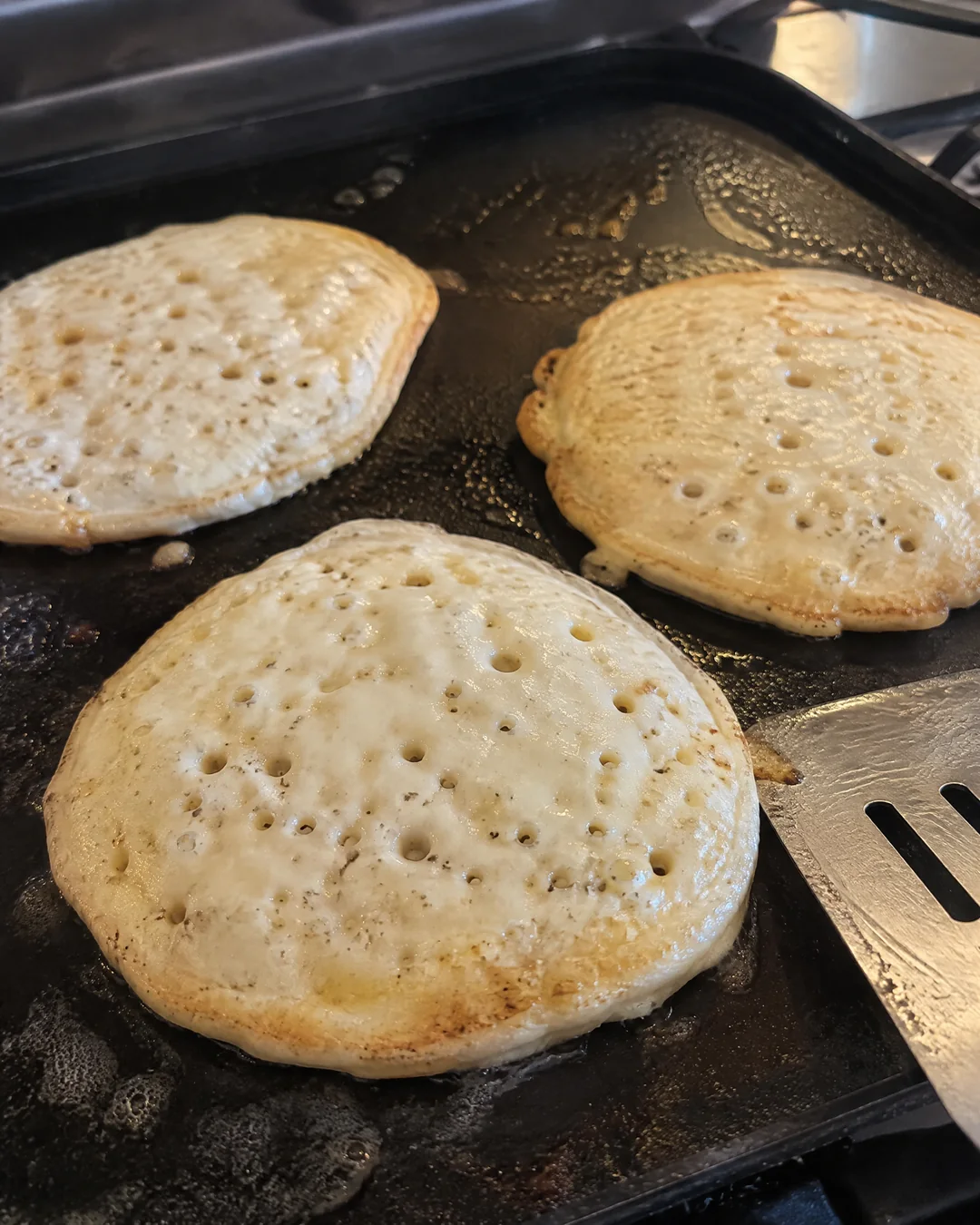 Pancakes on a griddle with bubbles popped and open, ready to flip