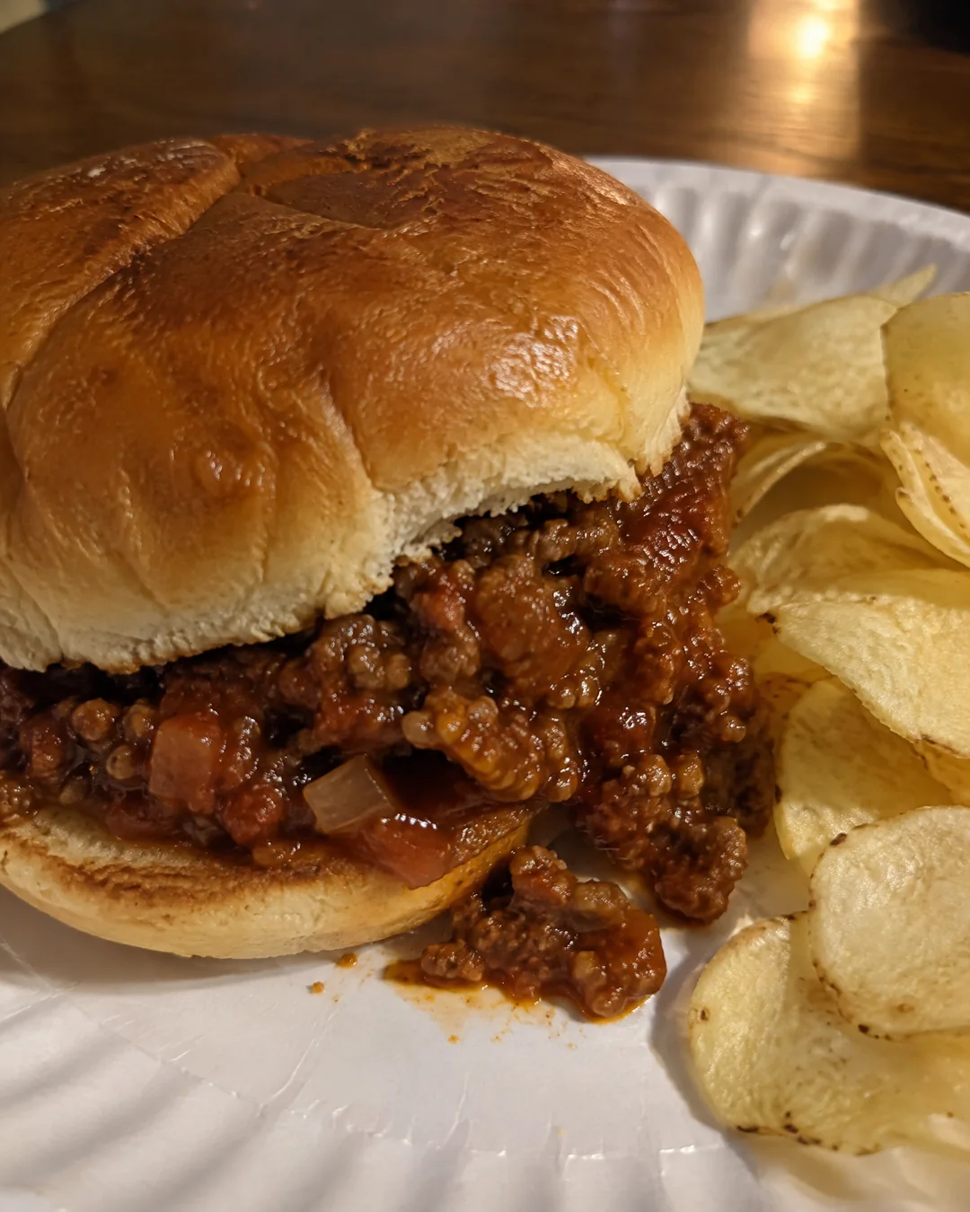 Sloppy joe on a toasted bun with the filling spilling onto a paper plate
