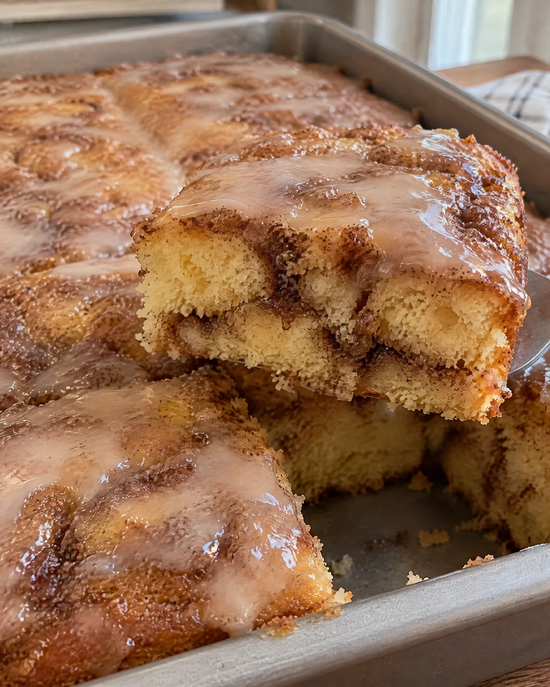Honey bun cake in its pan with vanilla glaze soaked in, one square cut out