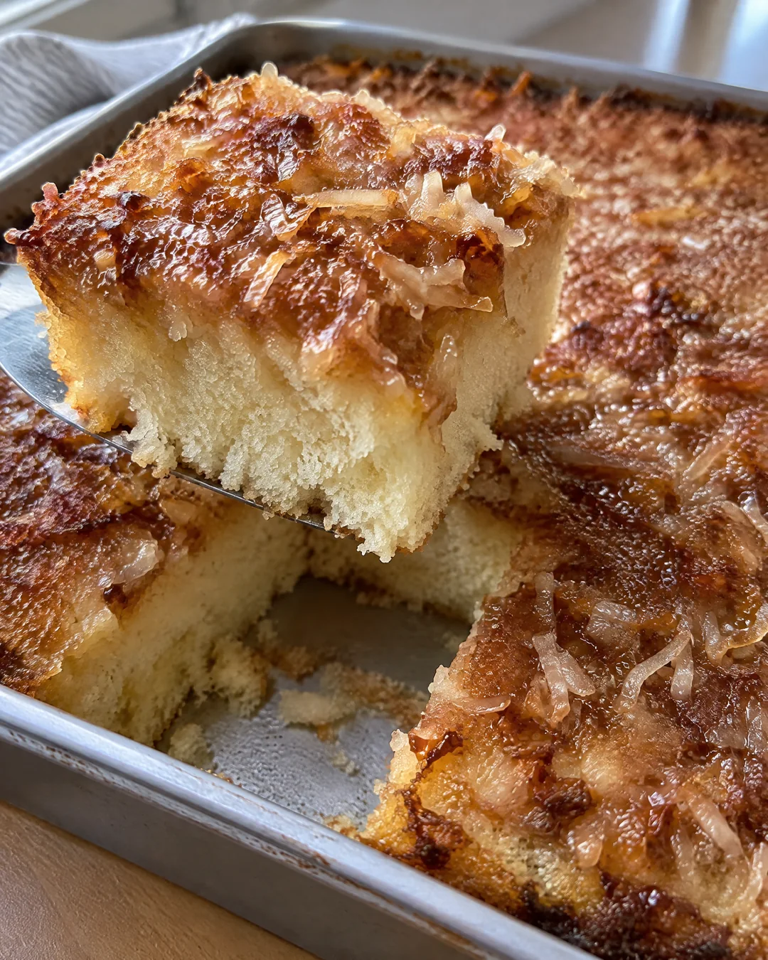 Hot milk cake in its square pan with broiled brown sugar coconut topping, one square cut out