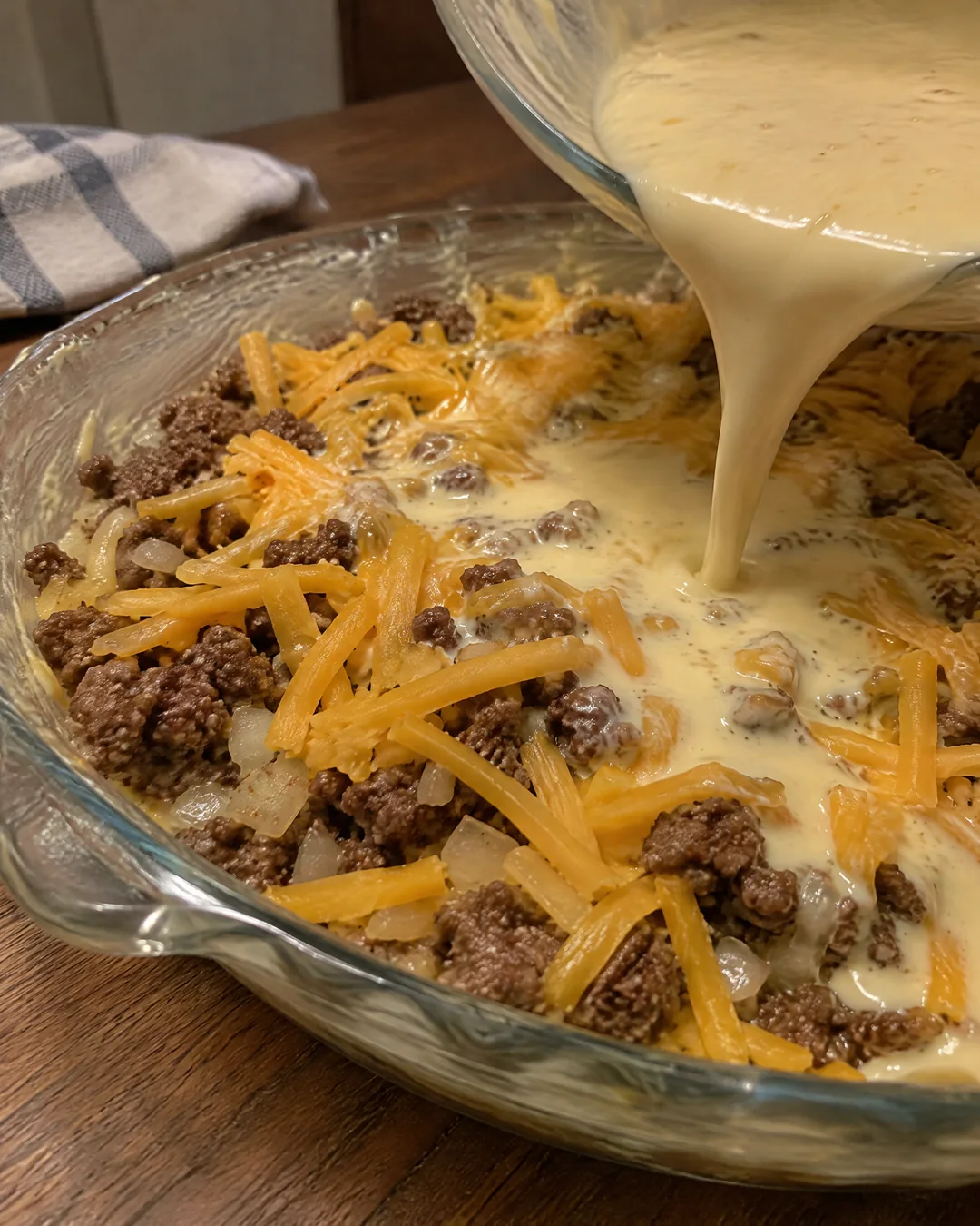 Batter being poured over beef and cheddar in a pie plate