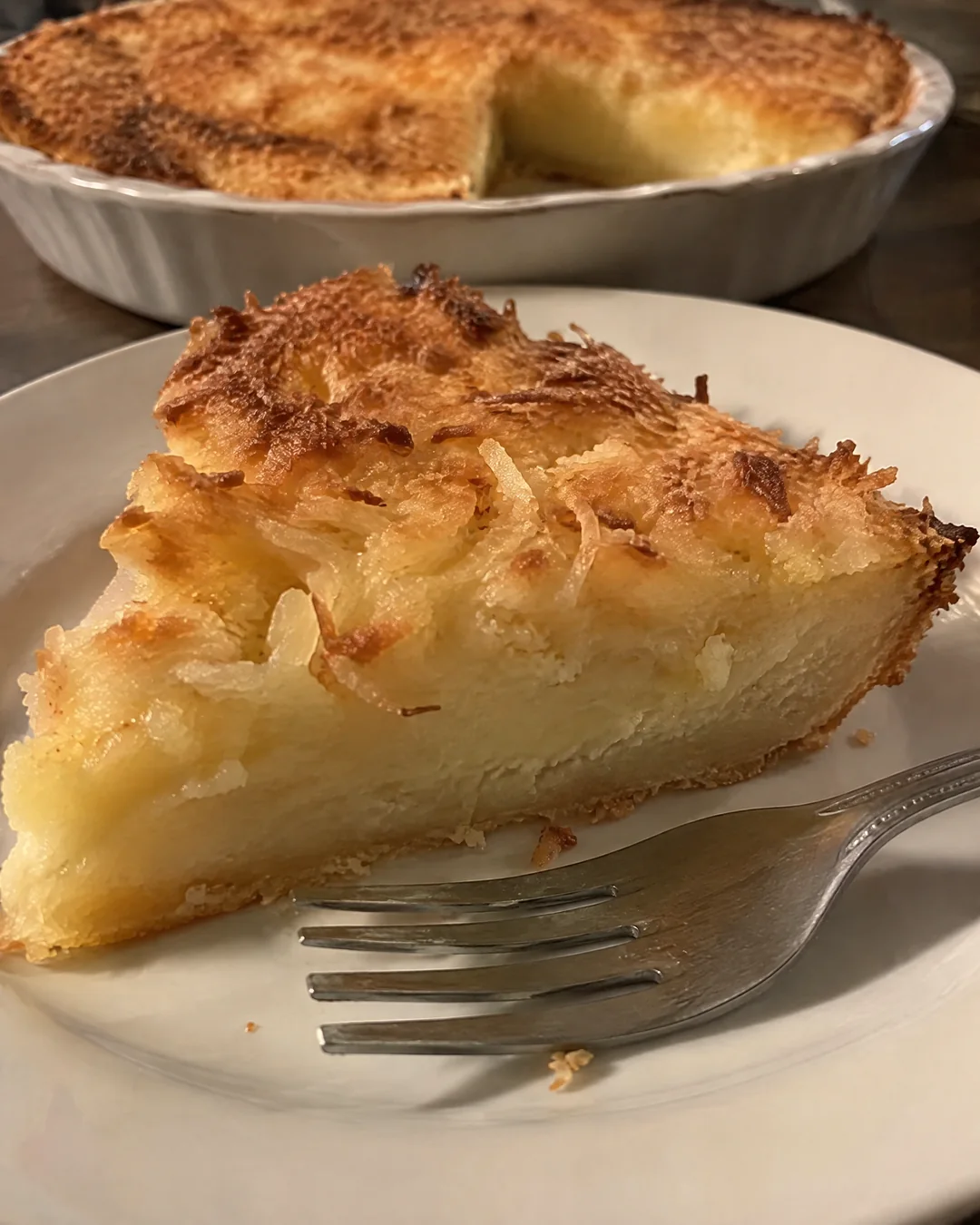 A wedge of impossible coconut pie on a plate showing the self-made crust, custard middle and toasted coconut top
