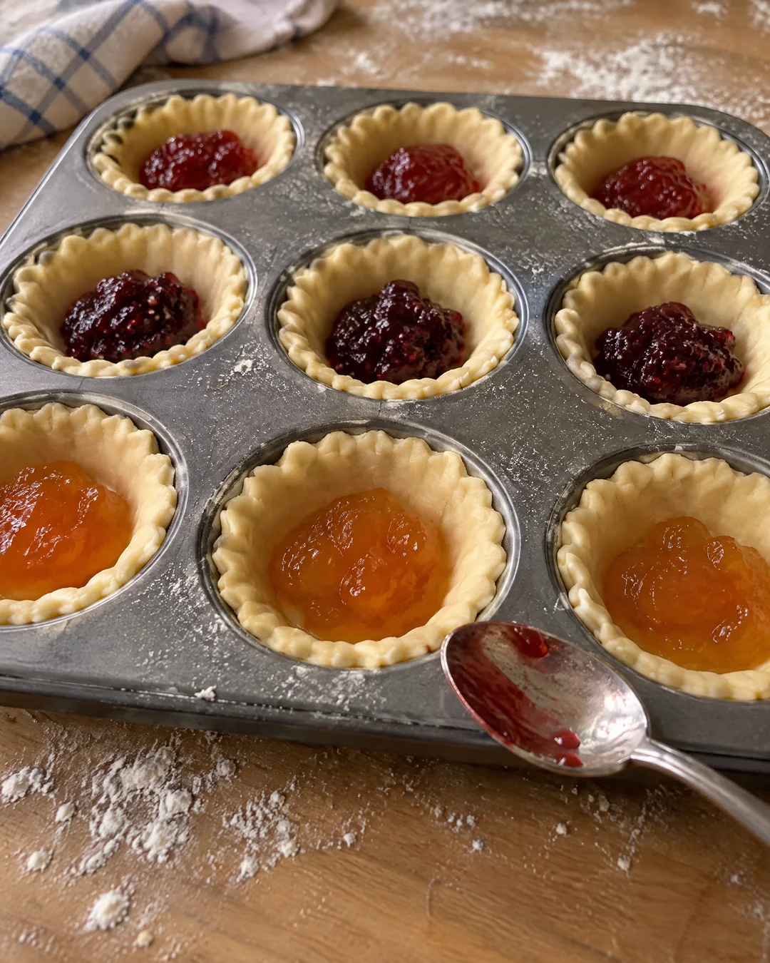 Shortcrust pastry rounds pressed into a bun tin with a teaspoon of jam in each