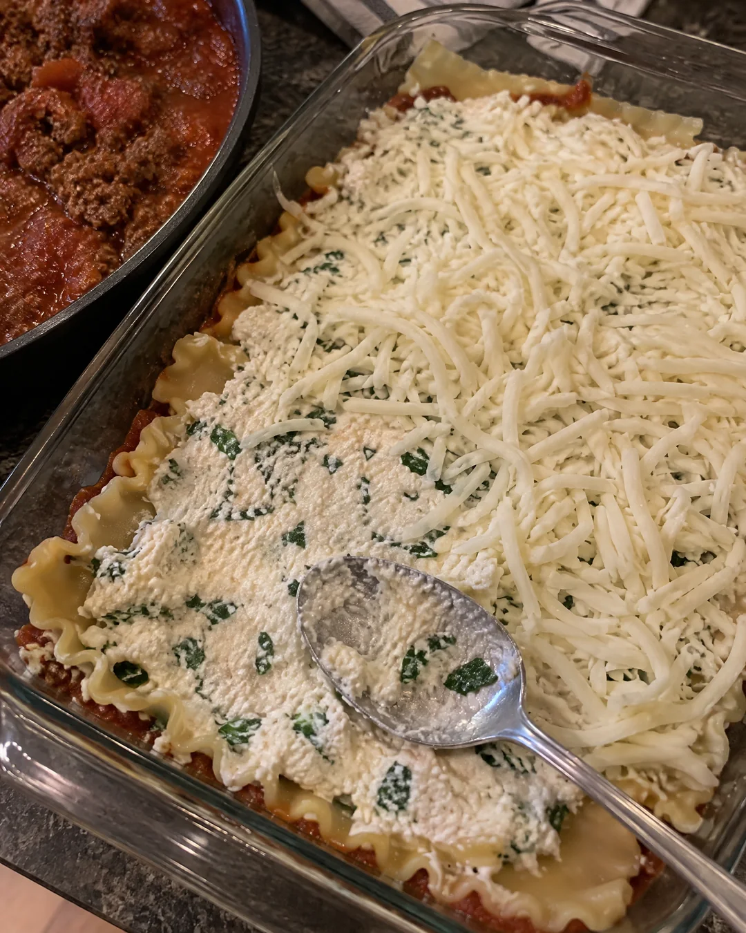 A half-built lasagna in a 9 by 13 dish with the cottage cheese layer spread over the noodles