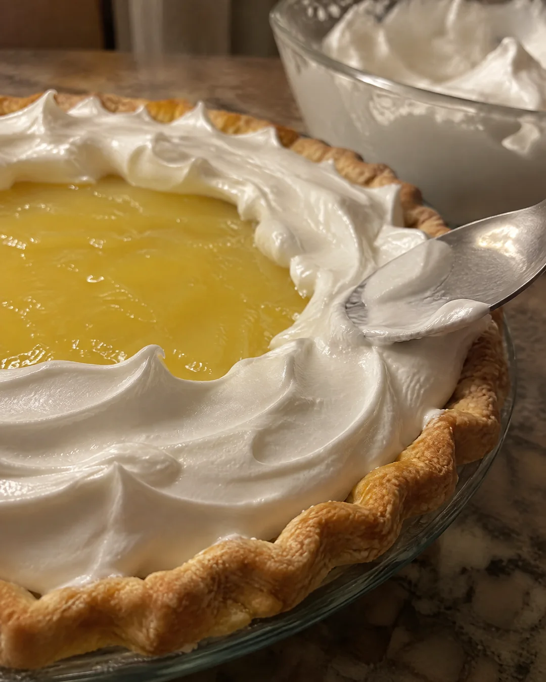 Meringue being spread over hot lemon filling and sealed to the edge of the pie crust