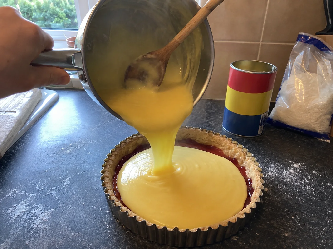 Pouring hot custard from the pan onto the jam-covered pastry case for a Manchester tart
