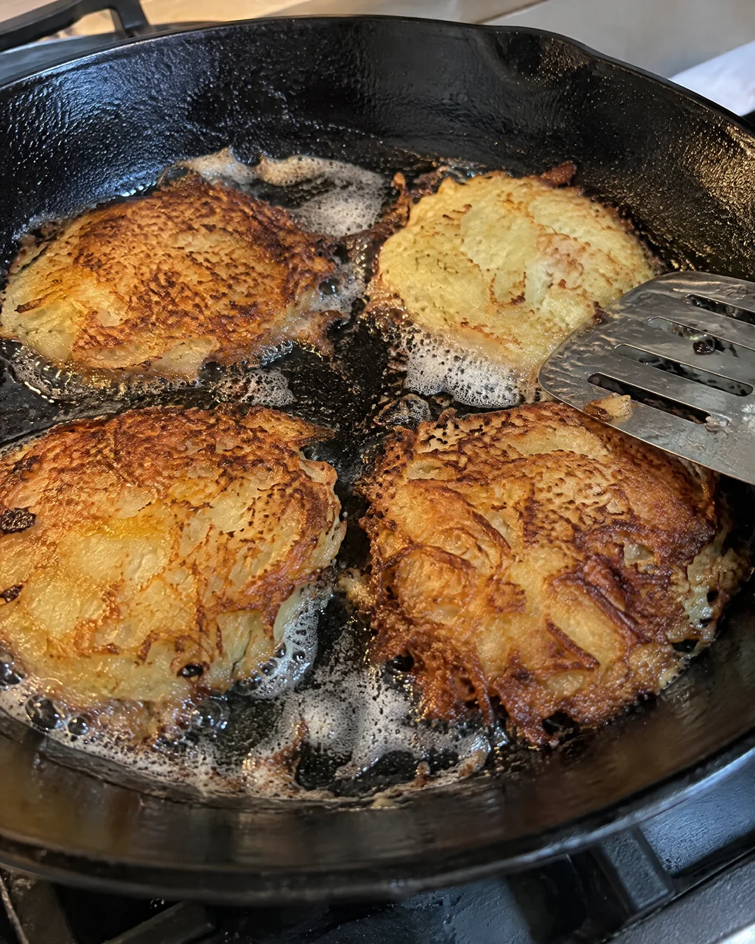 Mashed potato pancakes frying in a cast iron skillet