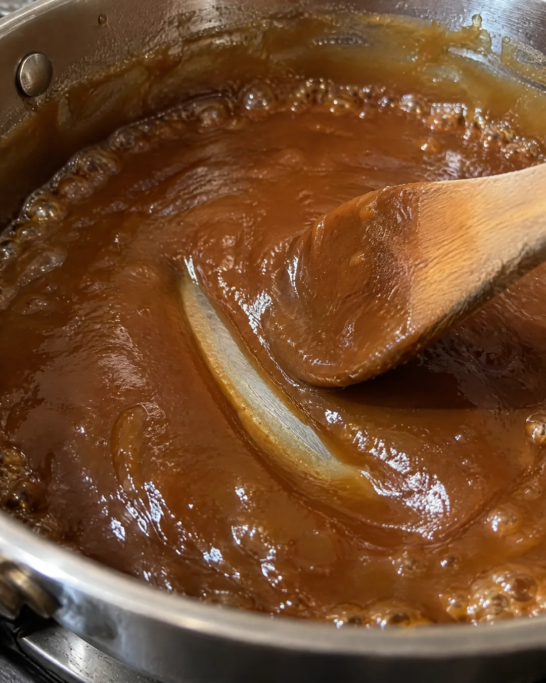 Thick fudge colored caramel being stirred in a saucepan