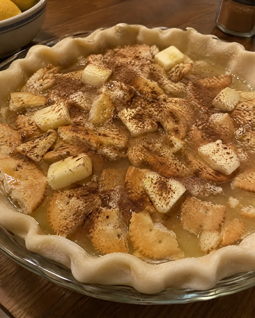 Broken round butter crackers floating in lemon syrup in an unbaked pie crust, dotted with butter and dusted with cinnamon