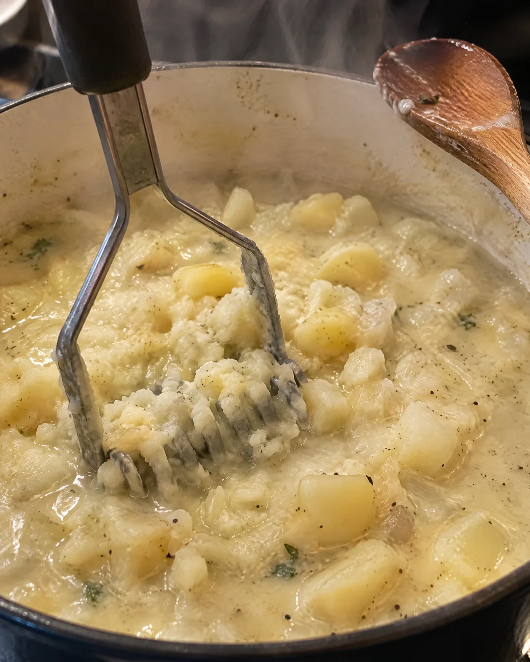 Potato masher pressing cooked potatoes into a pot of creamy soup