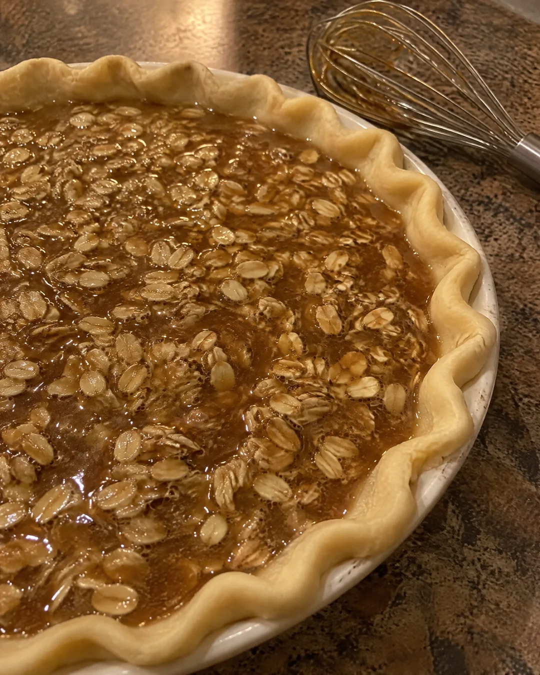 Oatmeal pie filling poured into an unbaked crust, the oats floating to the top of the glossy brown sugar syrup
