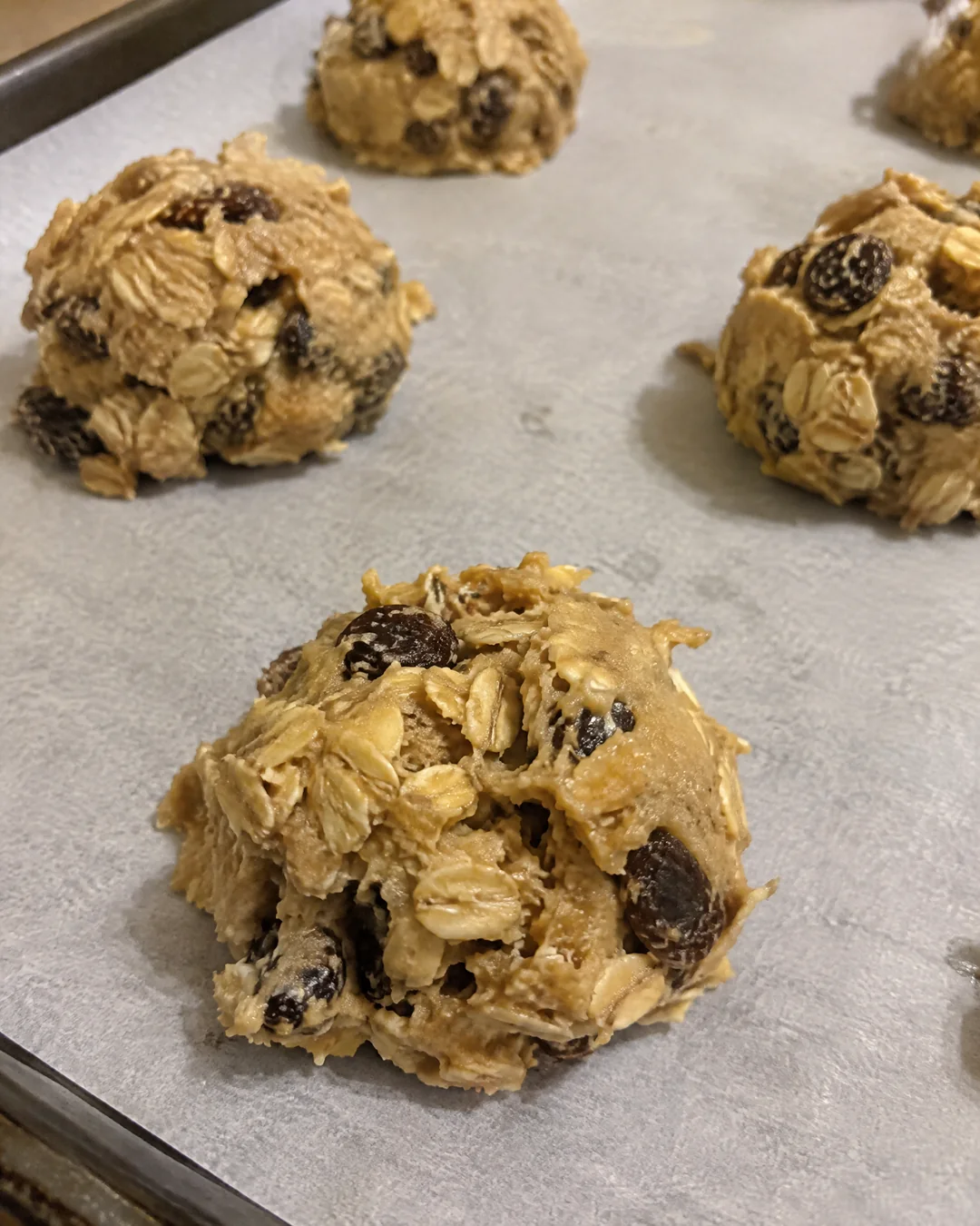 Scoops of oatmeal raisin cookie dough on a parchment-lined baking sheet before baking