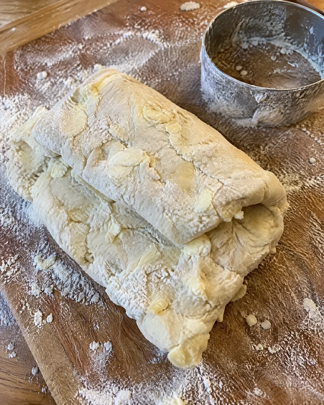 Biscuit dough patted into a rectangle on a floured board, shreds of grated frozen butter visible, folded over like a letter