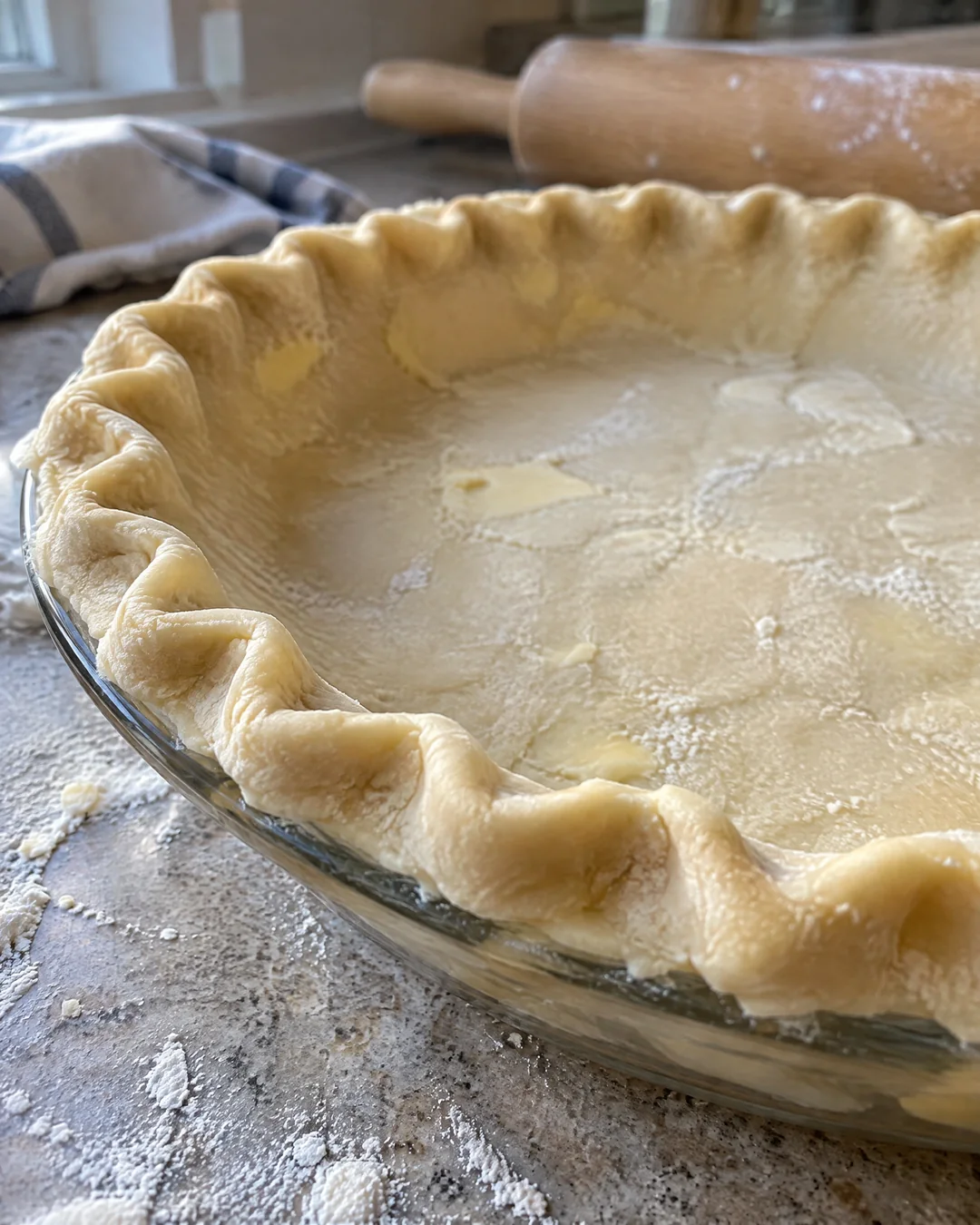 A crimped pie crust shell in a glass pie plate ready for the oven