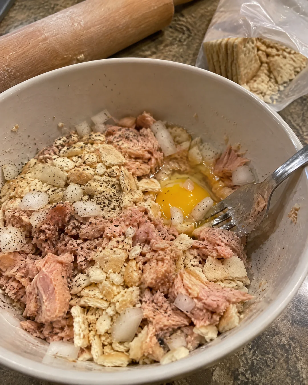 Canned salmon, crushed saltines, egg and onion mixed with a fork in a bowl