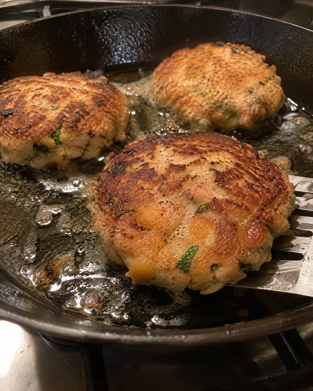 Salmon patties frying in a cast iron skillet, one turned to show the gold crust