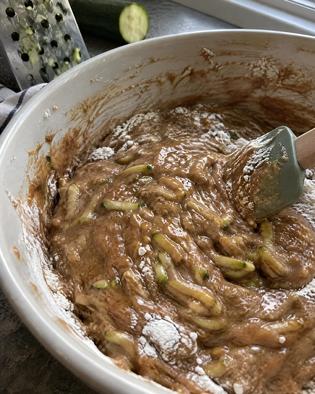 Thick zucchini bread batter flecked with green shreds being folded together in a large mixing bowl