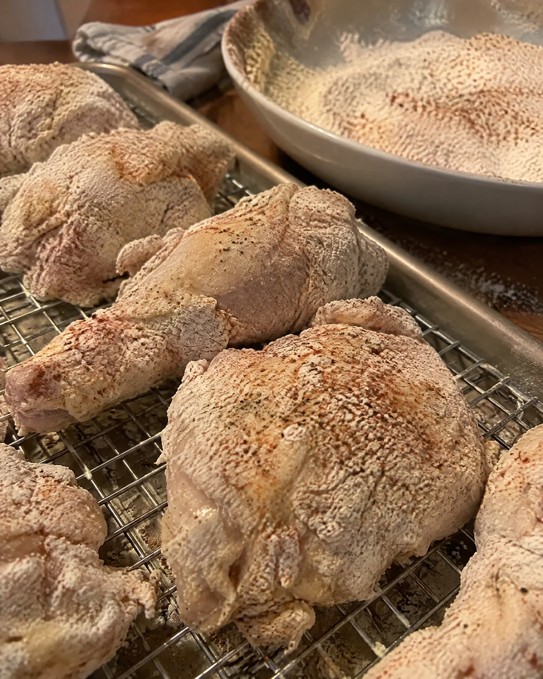 Floured buttermilk chicken pieces resting on a wire rack before baking