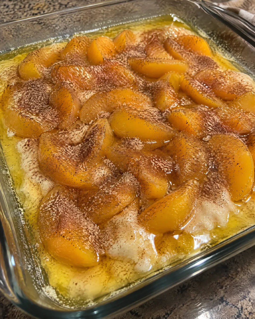 Batter poured over melted butter in a baking dish with peach slices spooned on top, unstirred