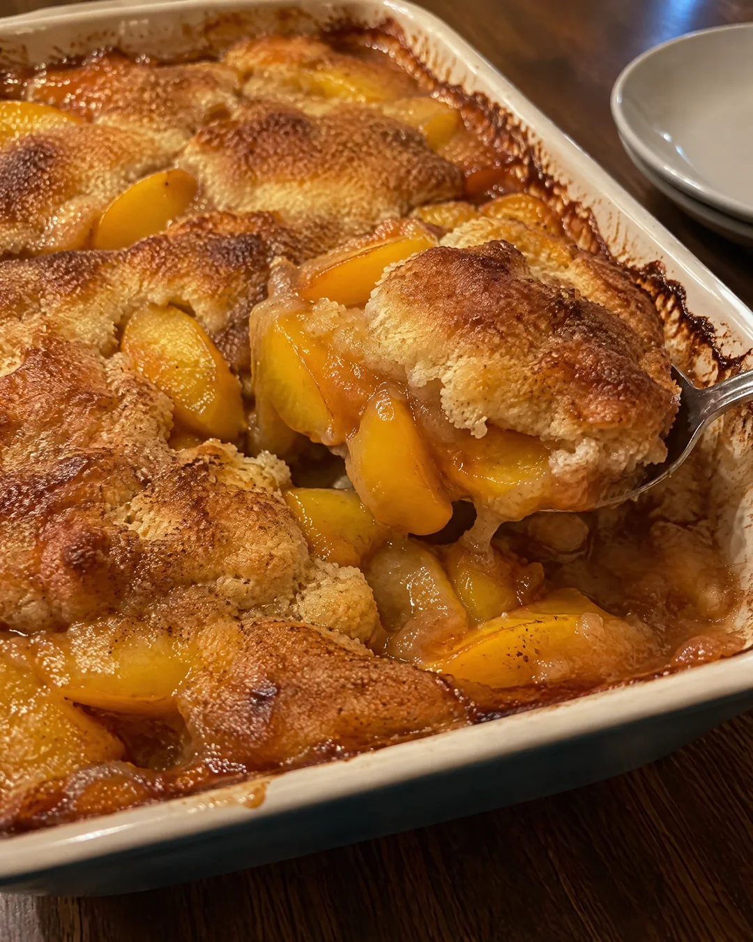 A baked peach cobbler with a golden crust risen up around the peaches, bubbling at the edges