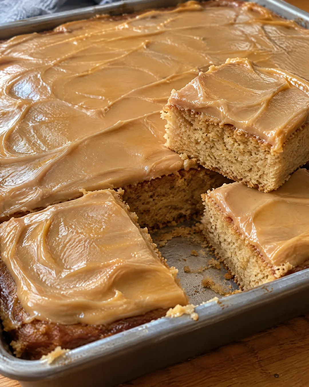 Peanut butter sheet cake with glossy frosting in the pan, a few squares cut out