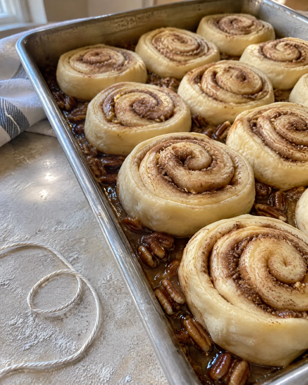 Rolled cinnamon dough sliced into rounds with thread, set on caramel and pecans in a baking pan