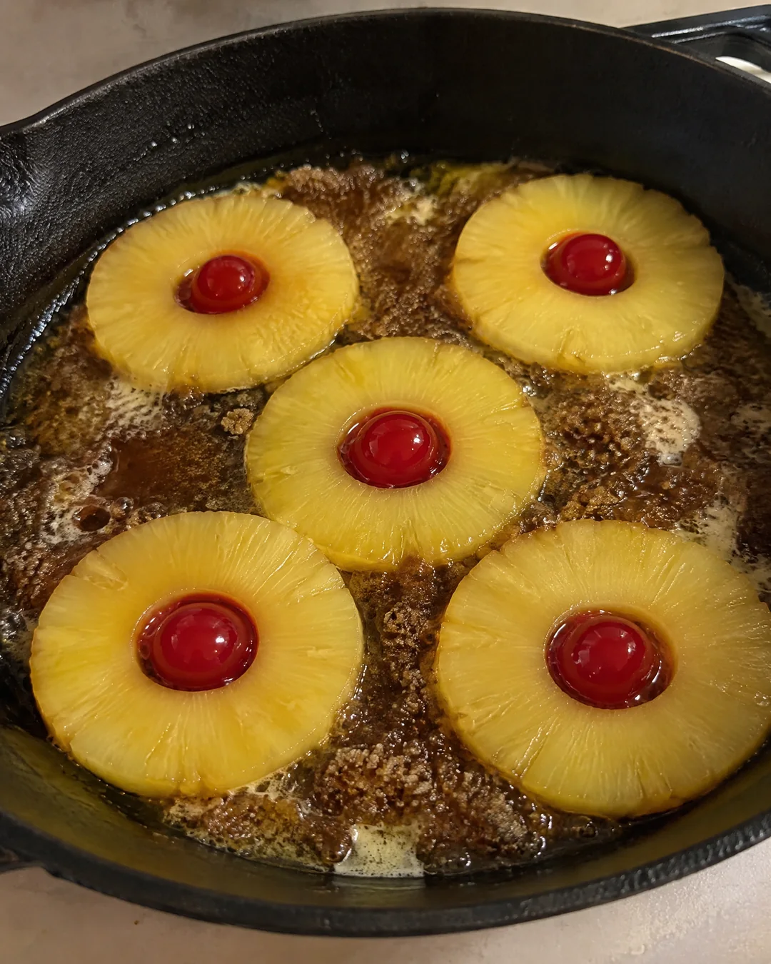 Pineapple rings and cherries arranged over brown sugar in a cast iron skillet