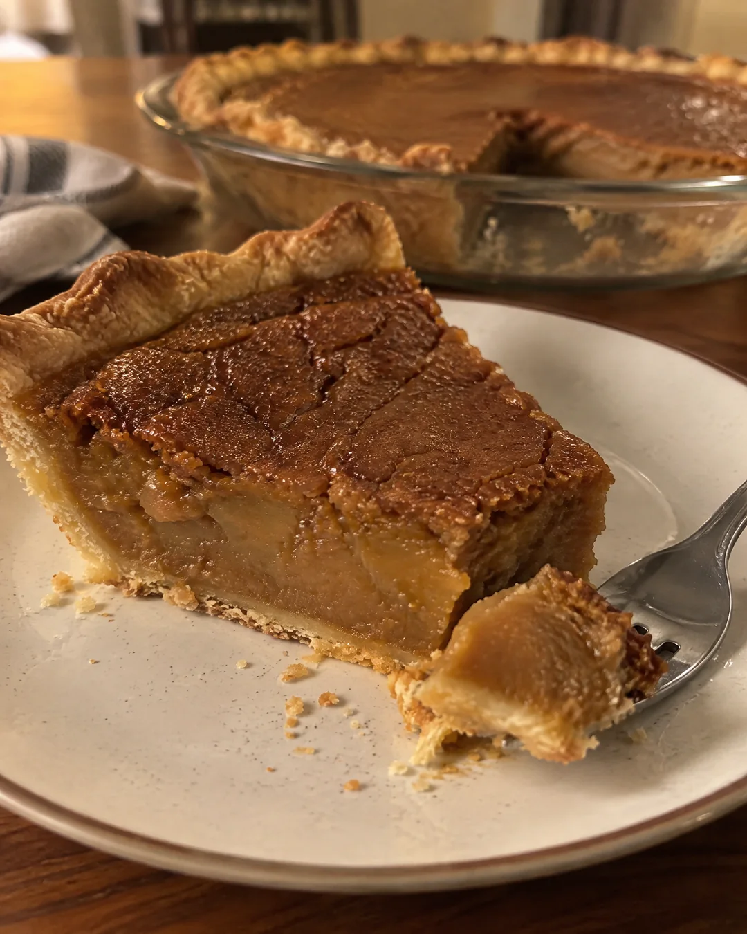 A wedge of baked pinto bean pie on a small plate, the brown crackled top and dense smooth filling showing at the cut edge