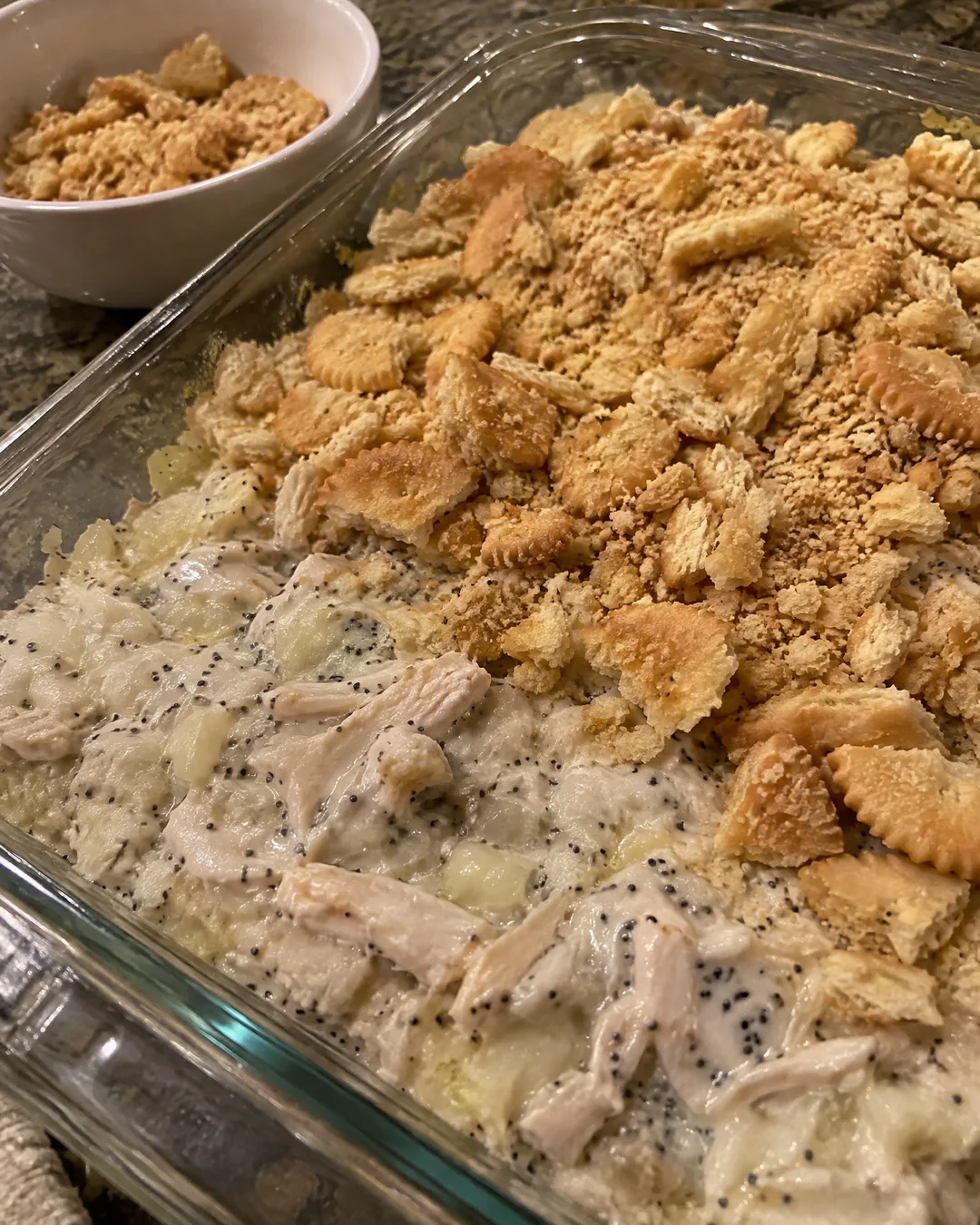 Unbaked poppy seed chicken casserole with buttered cracker pieces and poppy seeds scattered on top