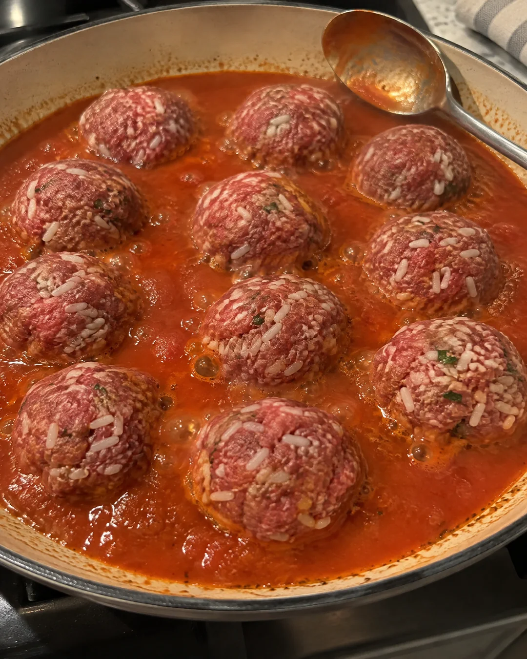 Raw porcupine meatballs studded with grains of uncooked rice sitting in thin tomato soup sauce in a skillet before the lid goes on