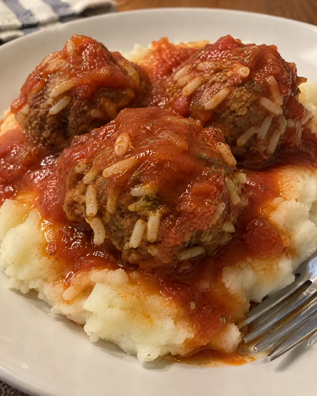 Cooked porcupine meatballs over mashed potatoes with swollen rice poking out like quills and thick tomato sauce spooned over