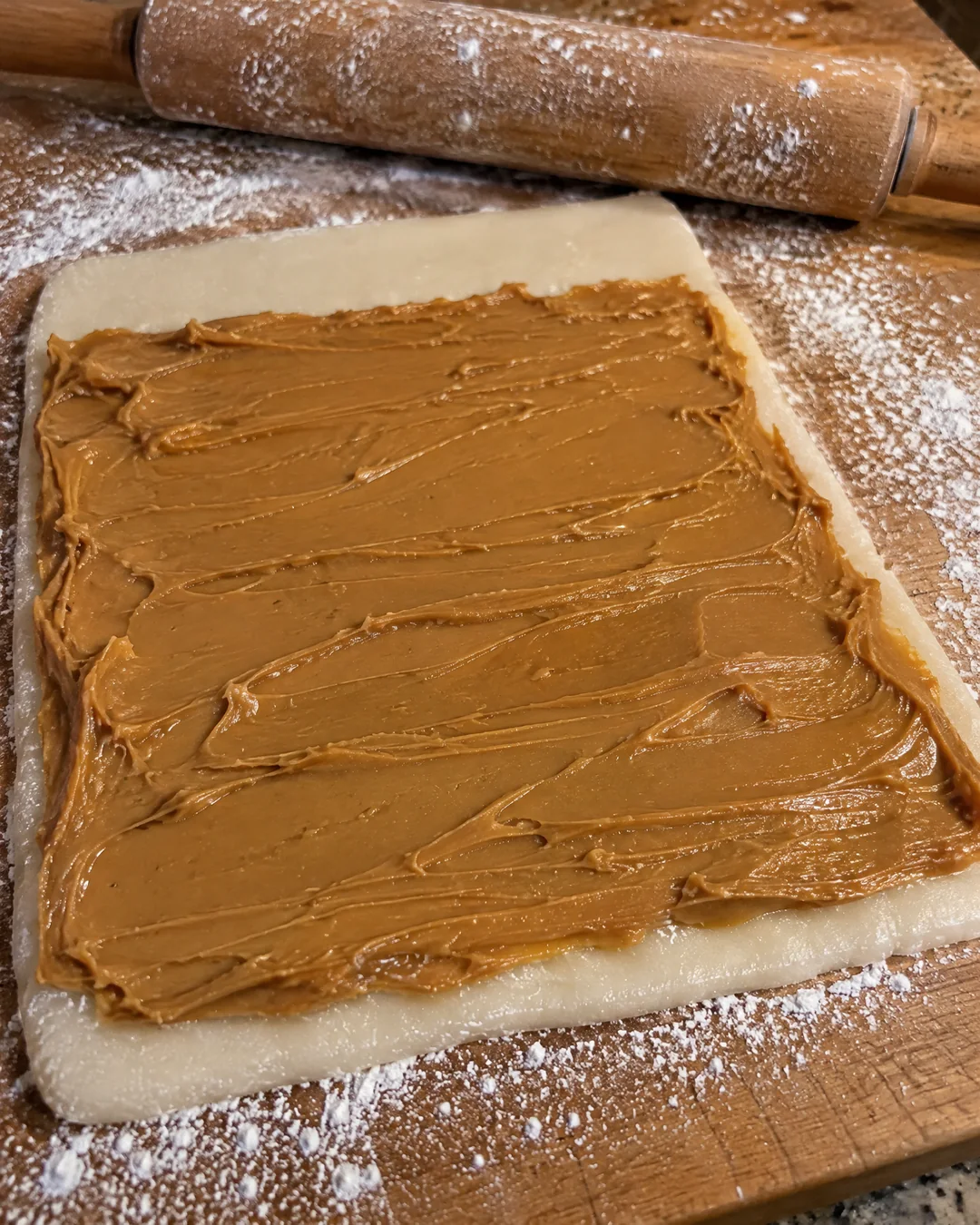 Potato candy dough rolled out on a sugar-dusted board and spread with a thin layer of peanut butter, ready to roll