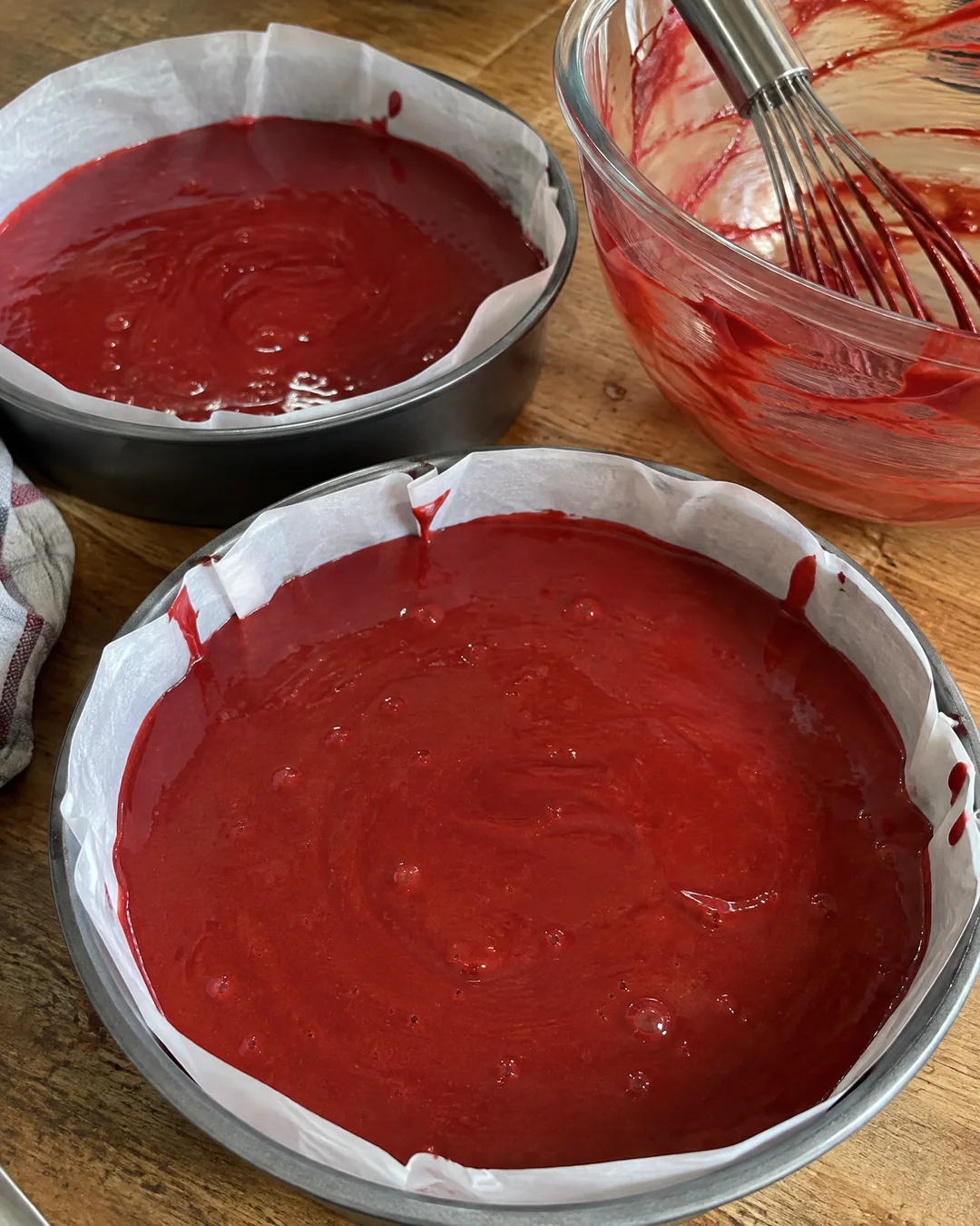 Glossy red velvet batter poured into two parchment-lined 9-inch round cake pans before baking