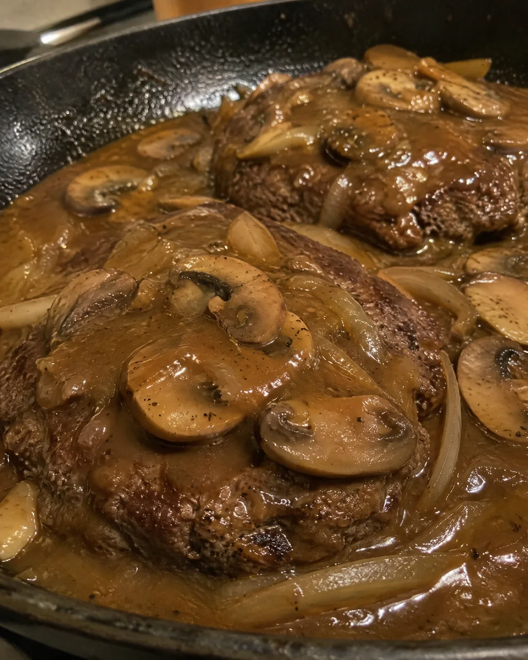 Salisbury steak patties simmering in mushroom and onion gravy in the skillet