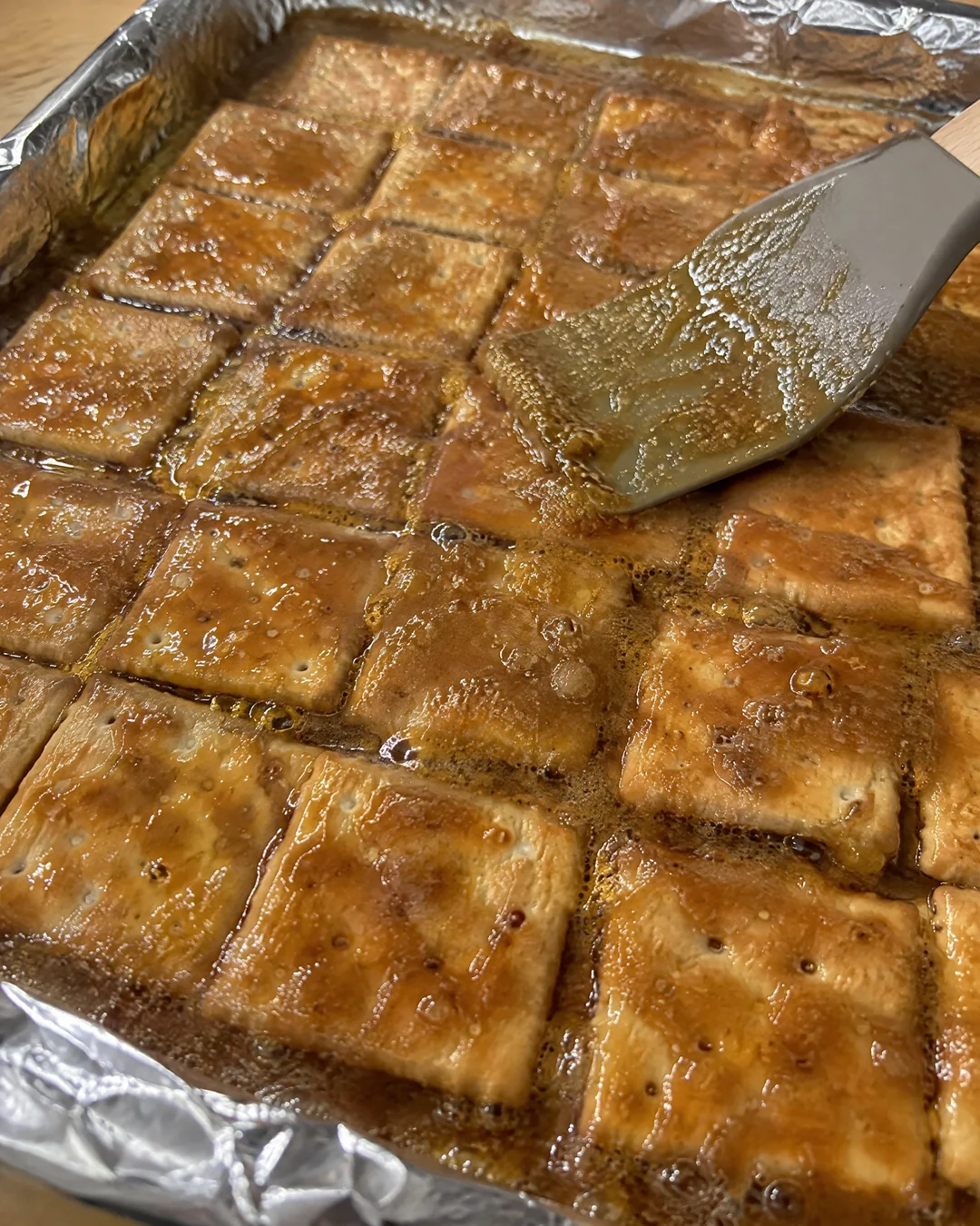 Bubbling butter toffee spread over a single layer of saltine crackers in a foil-lined pan