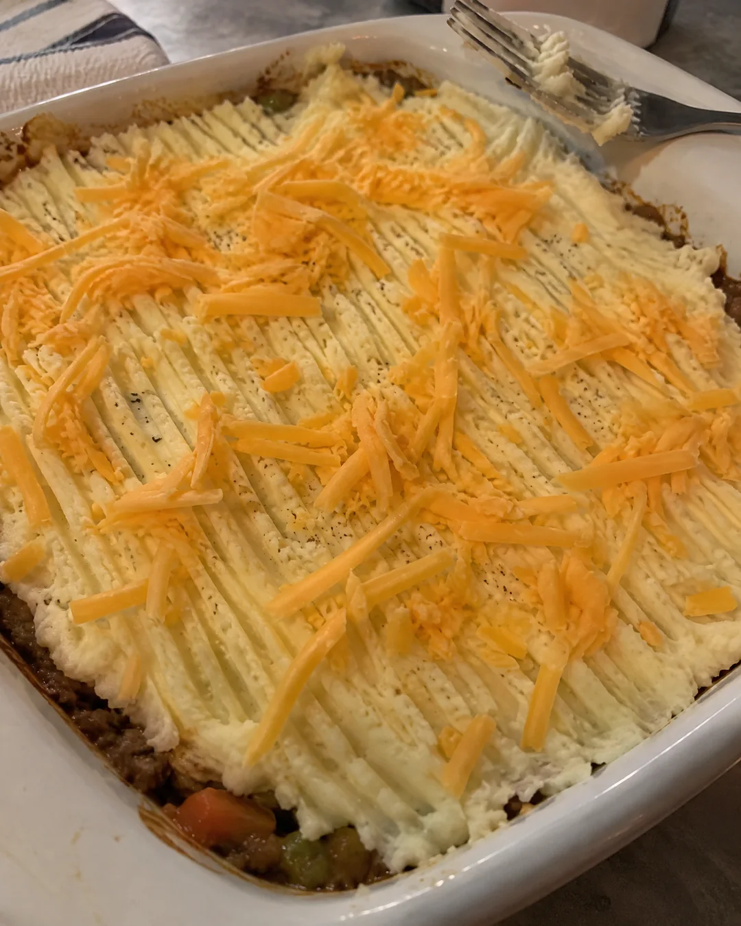 Unbaked shepherd's pie with the mashed potato top dragged into ridges with a fork and sprinkled with cheddar