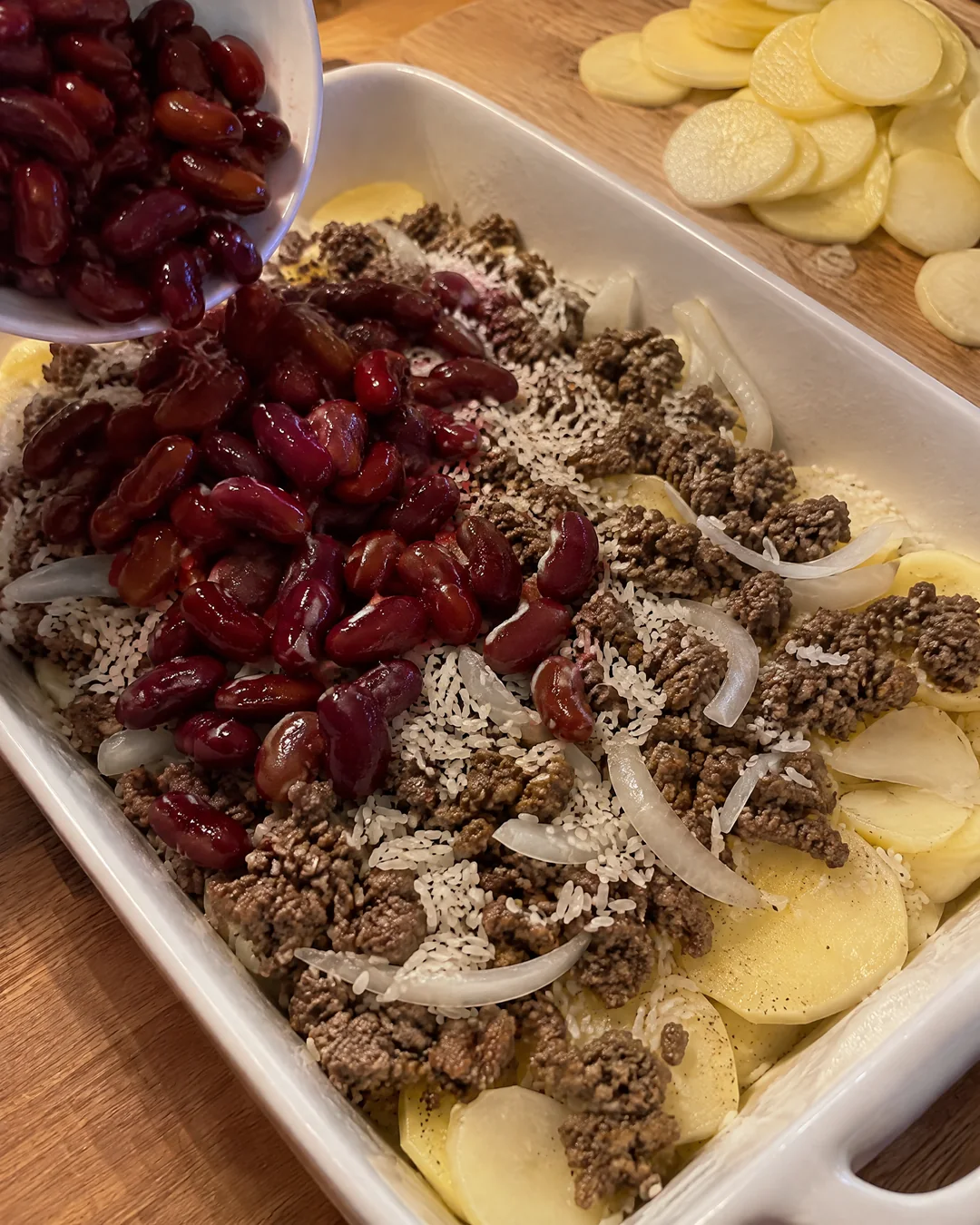 Layering potatoes, ground beef, rice and beans for shipwreck casserole