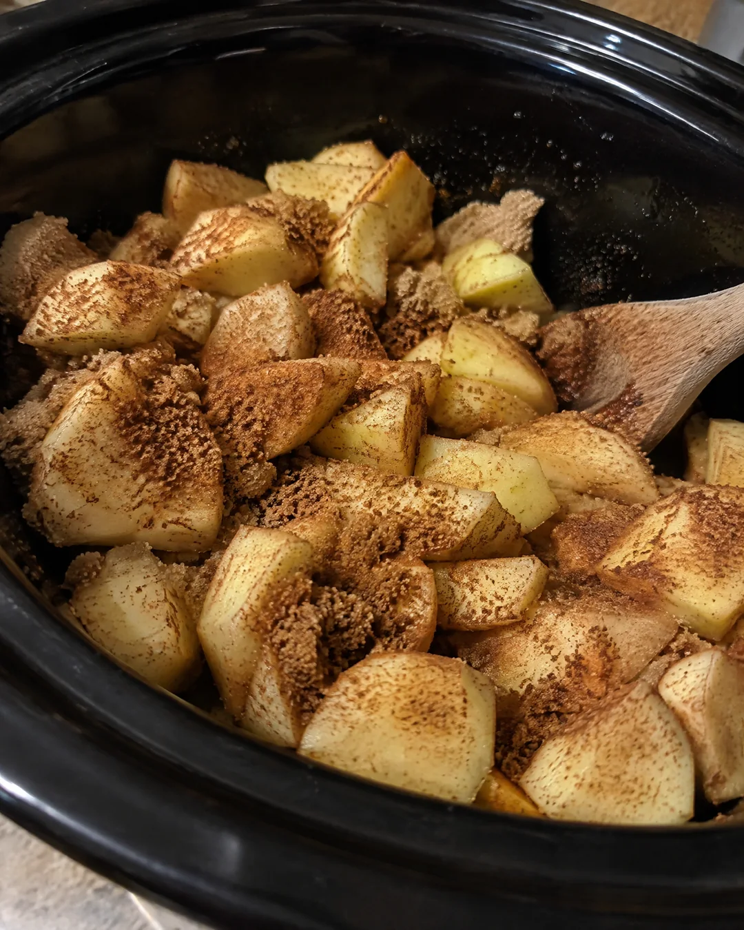 Chopped apples with brown sugar and spices in a slow cooker before cooking