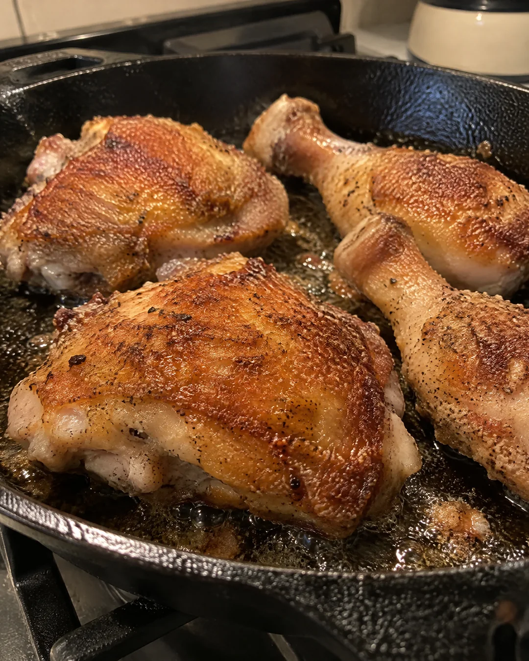 Chicken pieces browning skin side down in a cast iron skillet