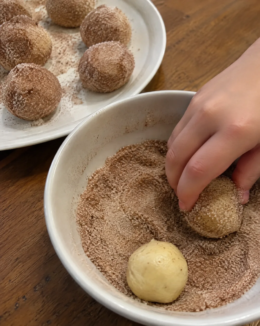 Rolling balls of snickerdoodle dough in a bowl of cinnamon sugar