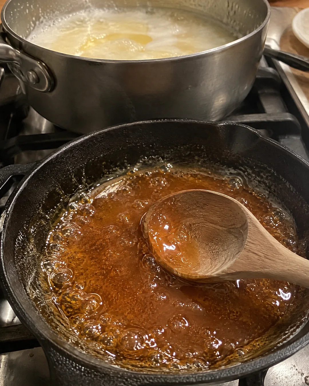 Amber melted sugar in a cast iron skillet beside a pot of boiling caramel icing base