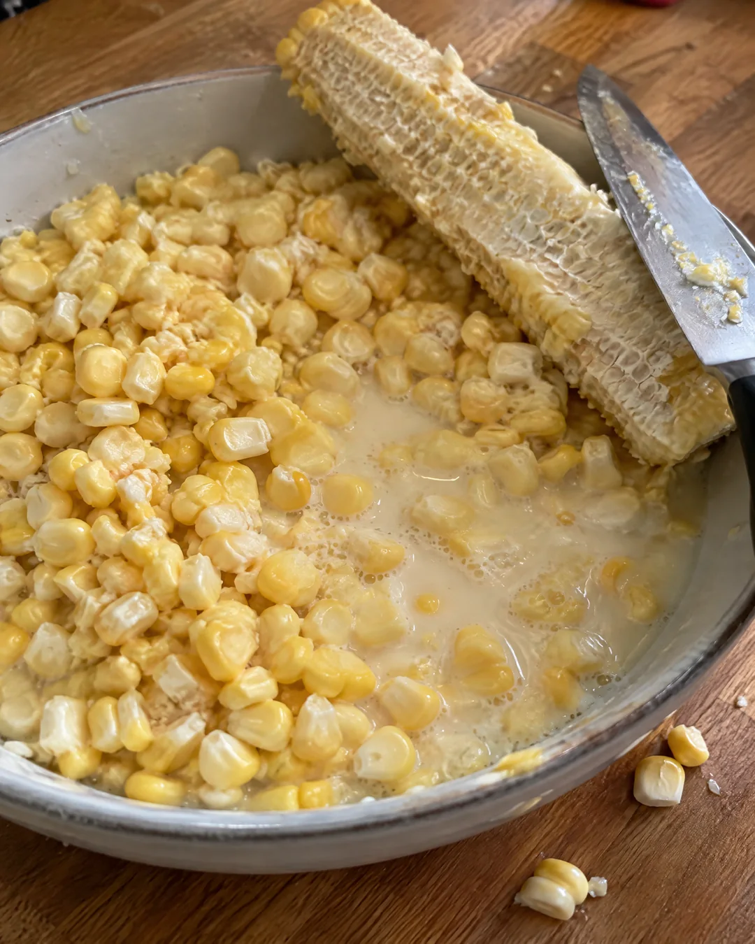 Fresh corn kernels cut shallow into a bowl with a bare cob scraped for its milky white starch