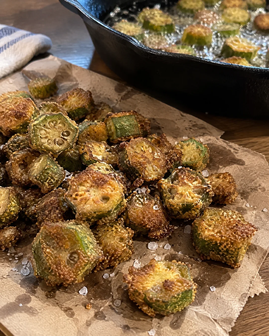 Golden fried okra draining on a brown paper sack beside the cast iron skillet, salted while hot