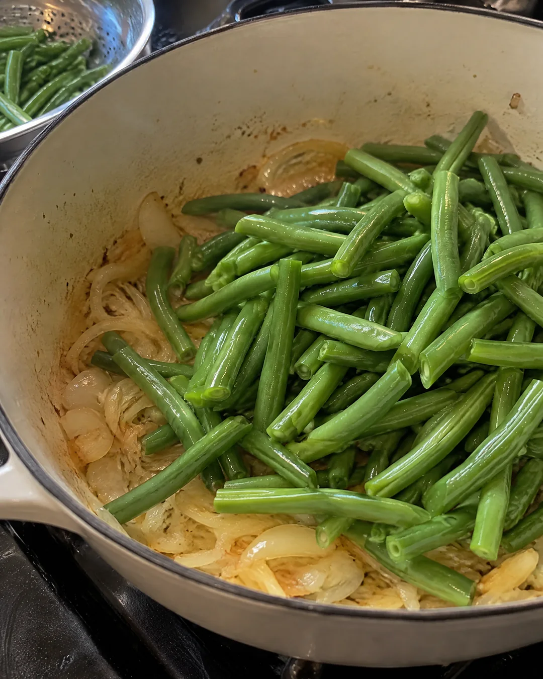 Snapped fresh green beans going into a heavy pot with butter and soft onion