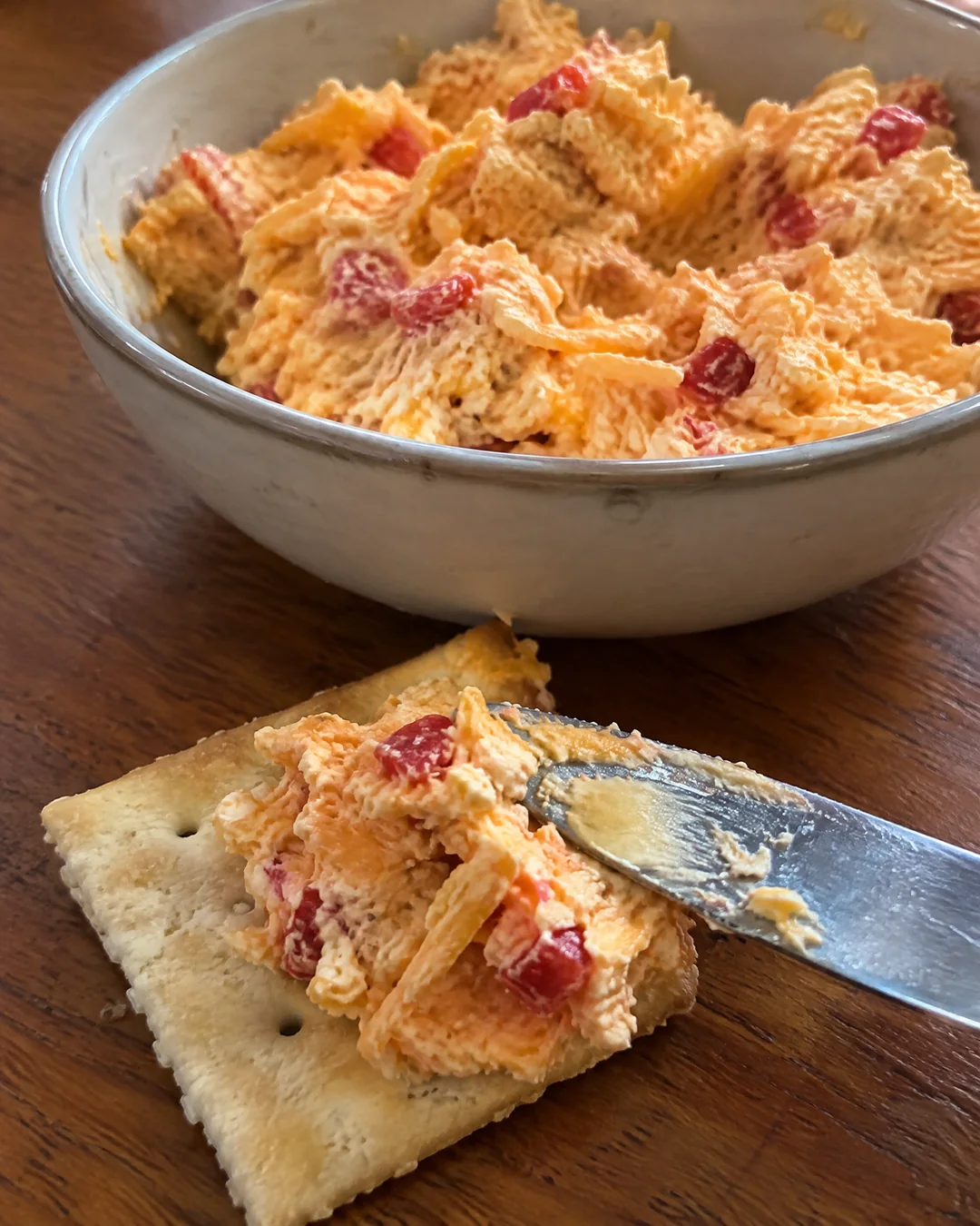 A bowl of homemade pimento cheese with a spreading knife and saltines
