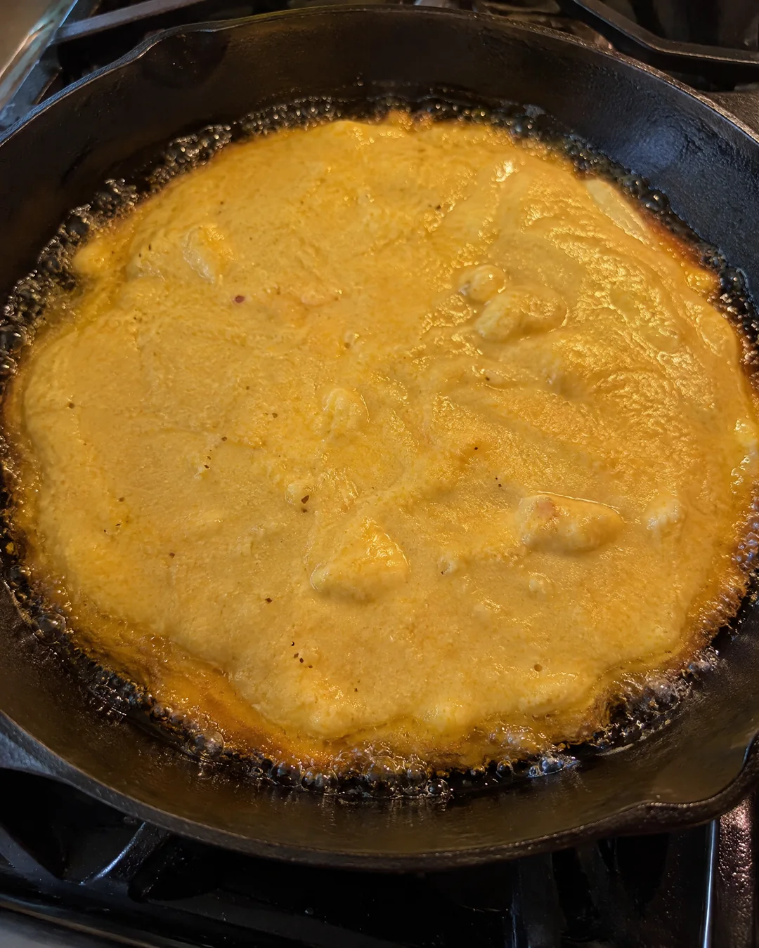 Cornbread batter just poured into a smoking hot cast iron skillet, the edges bubbling and frying in the fat