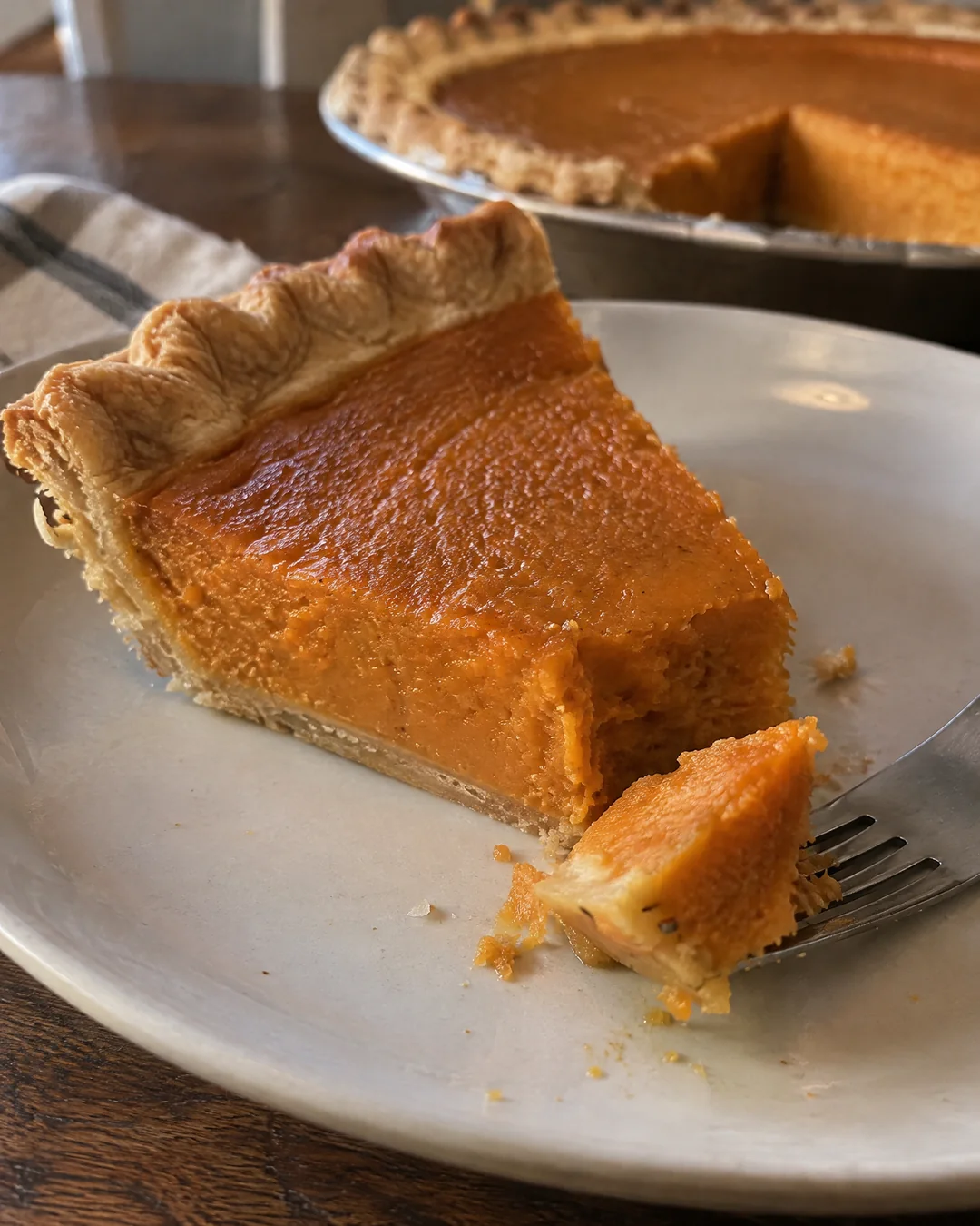A slice of Southern sweet potato pie on a plate, the deep orange smooth filling and fluted golden crust, the tip broken off by a fork