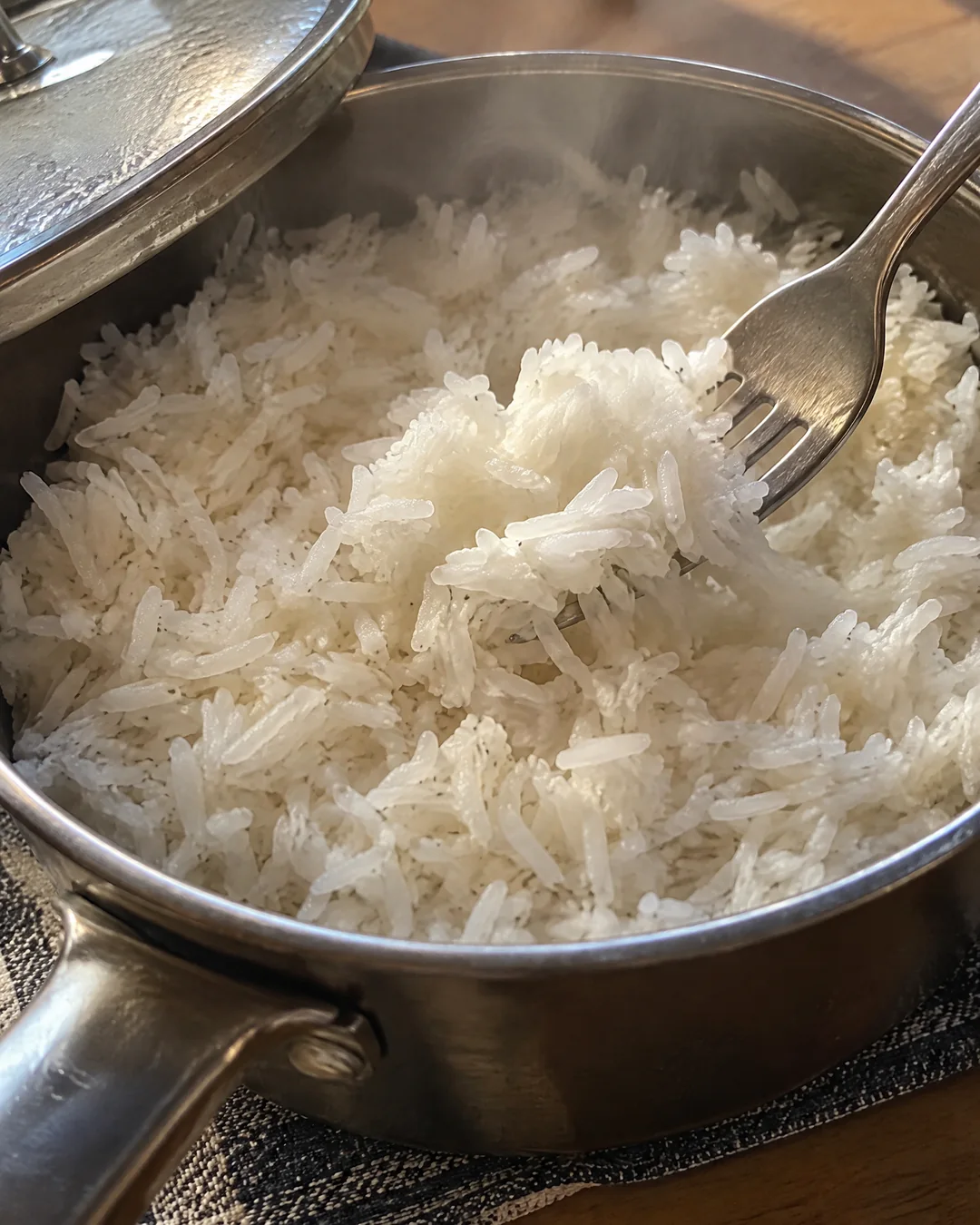 Fluffy cooked white rice in a saucepan being fluffed with a fork